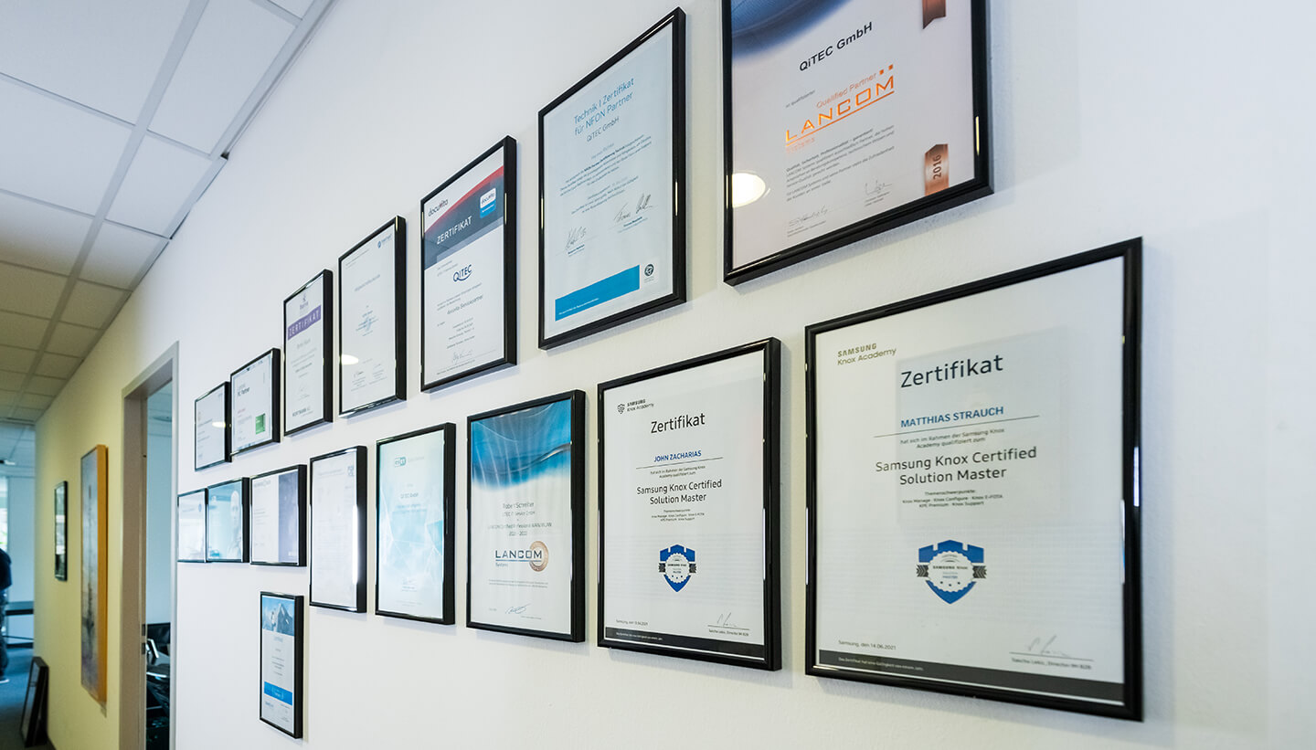 Wand mit gerahmten Partner- und Herstellerzertifikaten im QITEC-Büro